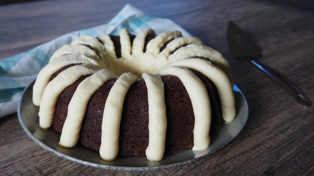 chocolate bundt cake with vanilla frosting on a dish towel on a wooden table