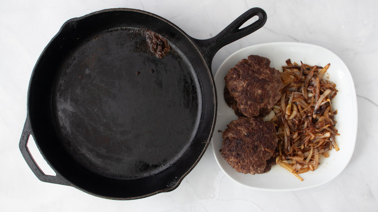 Skillet next to plate with burger patties and onions