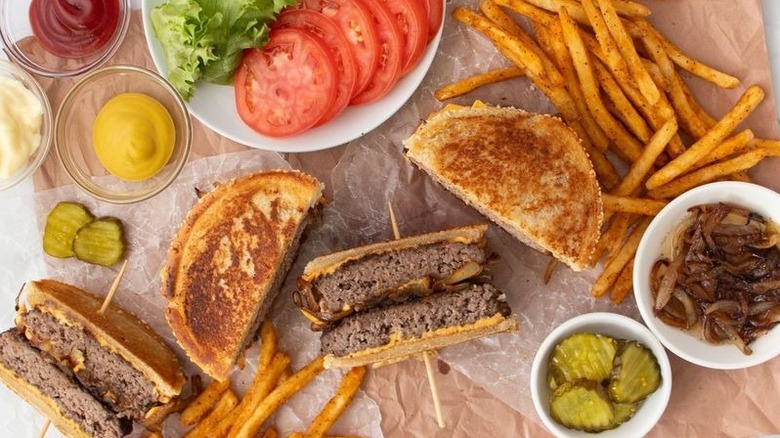 Halved patty melts with fries, tomatoes, lettuce, condiments, and pickles