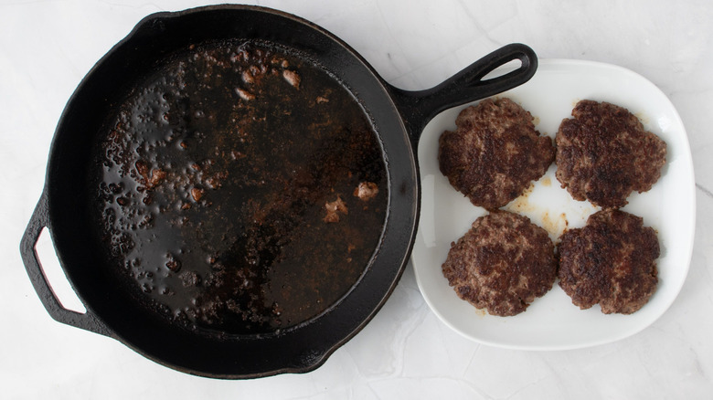 Skillet with drippings next to plate with patties