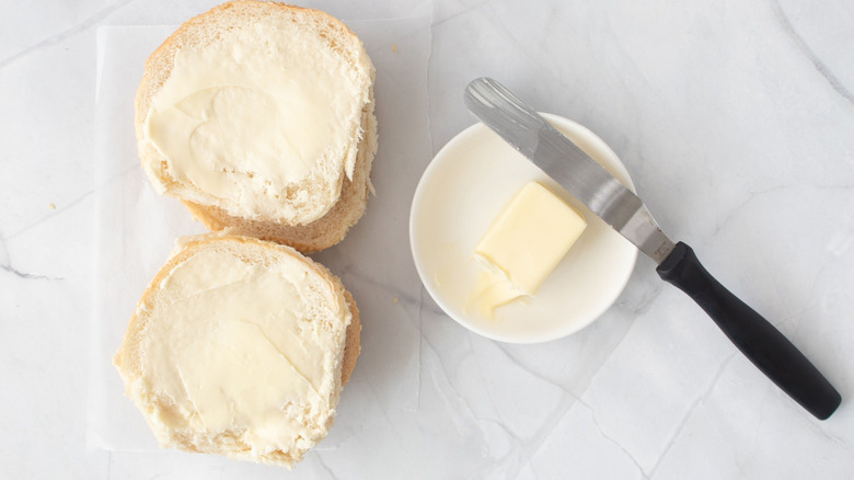 Buttered buns next to bowl of butter and knife