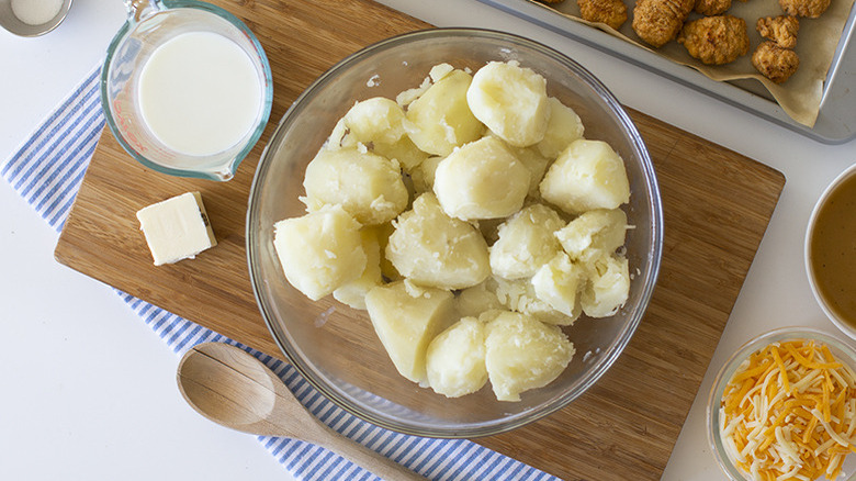Cooked potatoes in a bowl beside milk and butter