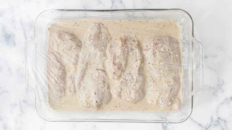 Marinating chicken in baking dish covered with plastic wrap