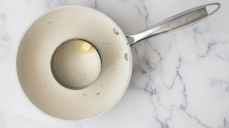 Melting butter inside a metal ring mold inside a white frying pan