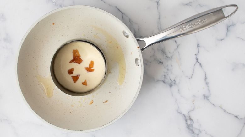 Batter with solidified syrup bits inside a metal ring mold inside a white frying pan