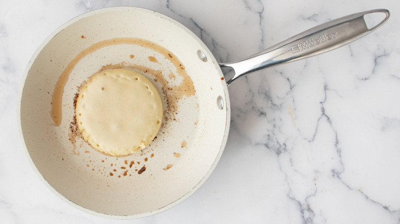 Partially cooked pancake inside a metal ring mold inside a white frying pan