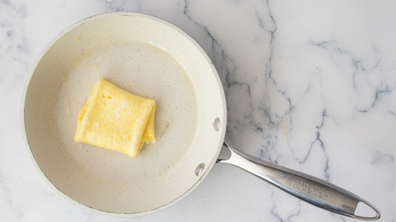 Folded cooked eggs in a white frying pan