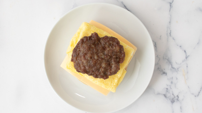 American cheese, cooked egg, and sausage patty on a white plate