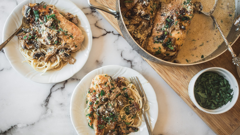 two plates of chicken marsala with spaghetti and large pan