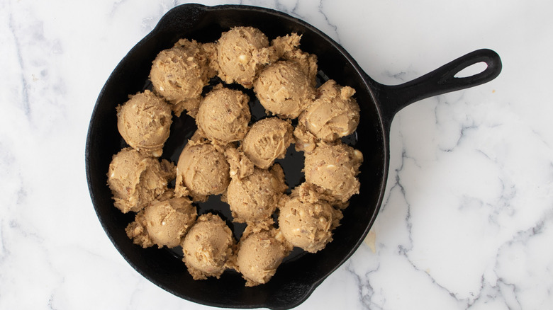 Balls of brown cookie dough in a cast iron frying pan