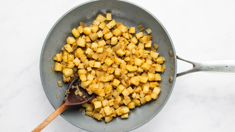 Sauteed cubed potatoes and diced onion in frying pan