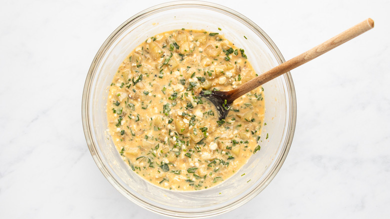 Egg, cheese, chive, and potato mixture in glass mixing bowl