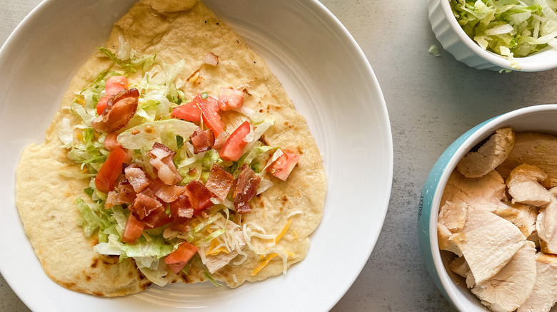 A chalupa sitting on a plate with bacon bits, lettuce, and cheese