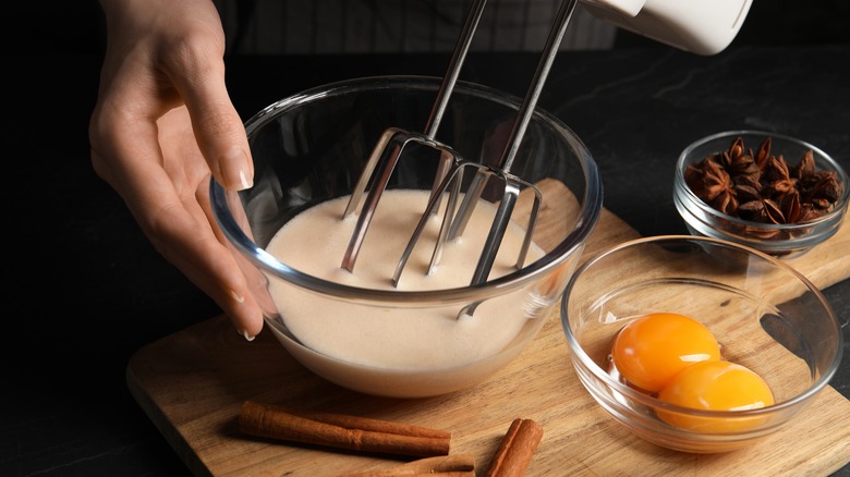 Person blending eggnog with bowl of egg yolks