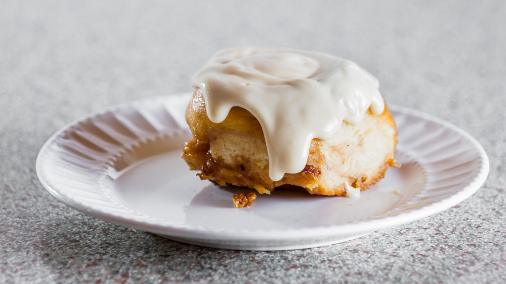 Cinnamon roll drenched in icing on a white plate