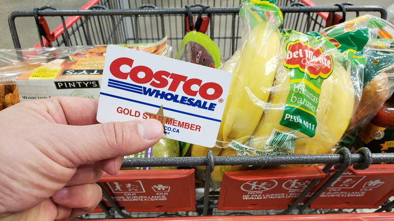 Costco shopper holding membership card in front of full cart