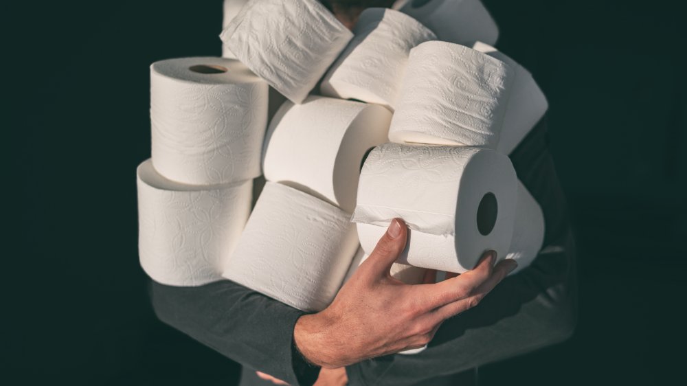 person with an arm full of toilet paper rolls