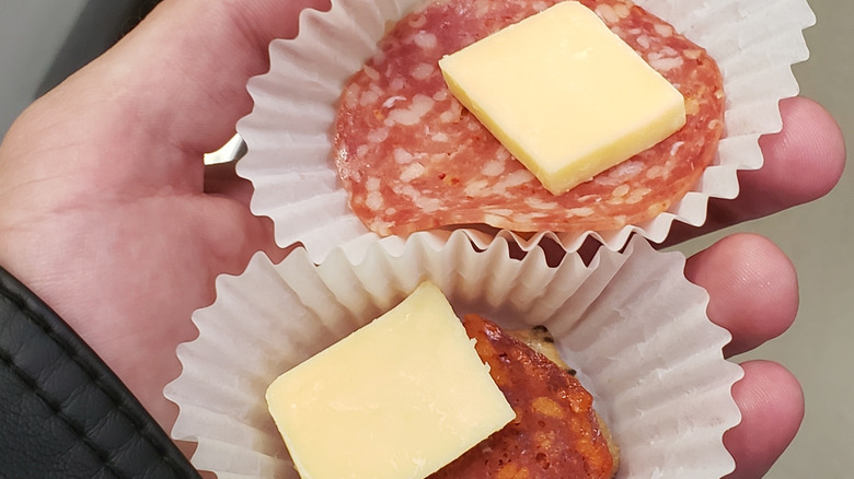 Hand holding two free samples of meat and cheese