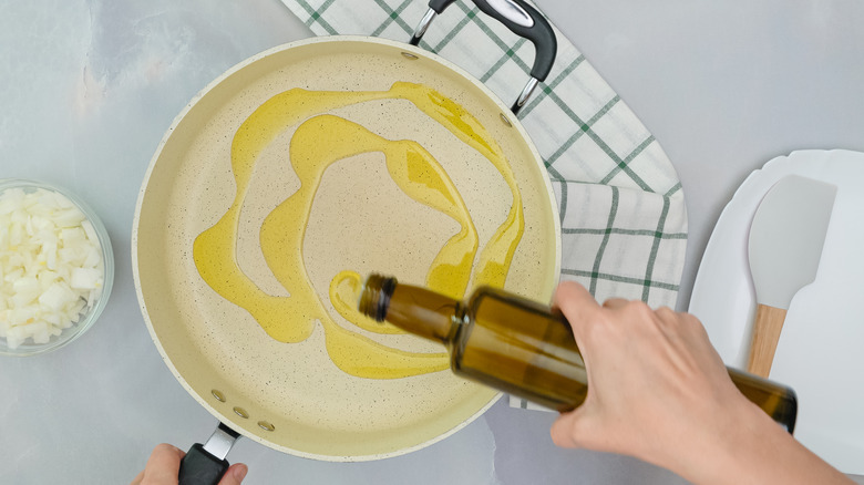 Hand pouring olive oil into pan