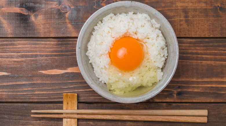 A raw egg over rice and chopsticks