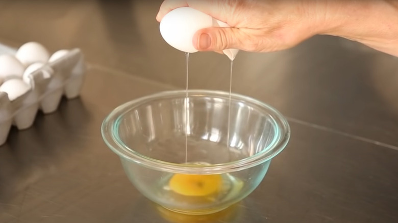 Hand holding eggshells with egg below in bowl