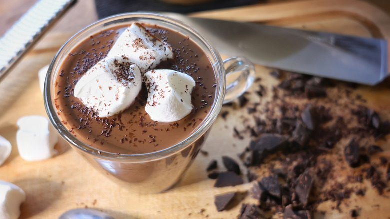 glass mug of dark hot chocolate on cutting board with marshmallows and chocolate chunks