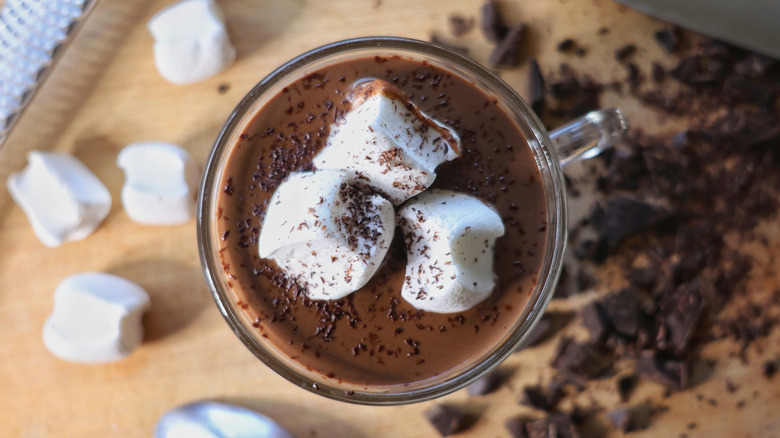 mug of hot chocolate on cutting board surrounded by marshmallows and chocolate chunks