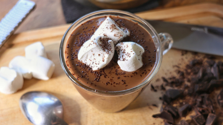 glass mug of hot cocoa with marshmallows and grated chocolate on top