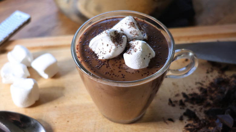 glass mug of dark hot chocolate with marshmallows on cutting board