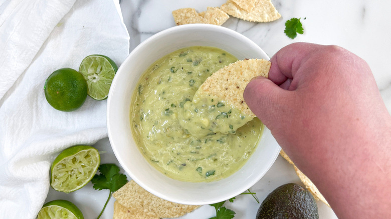 Hand dipping tortilla chip into salsa verde