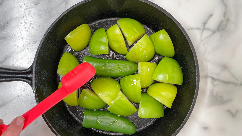 Measuring spoon pouring over tomatillos and jalapenos in pan