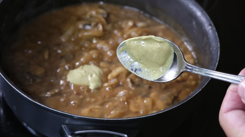 spooning mustard into skillet of sauce
