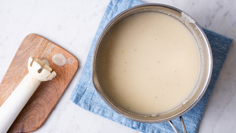 Creamy cauliflower soup in a pot next to an immersion blender