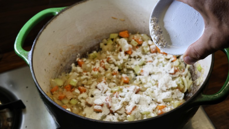 pouring flour into pot of vegetables