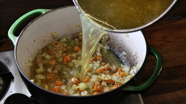 pouring broth into pot of vegetables