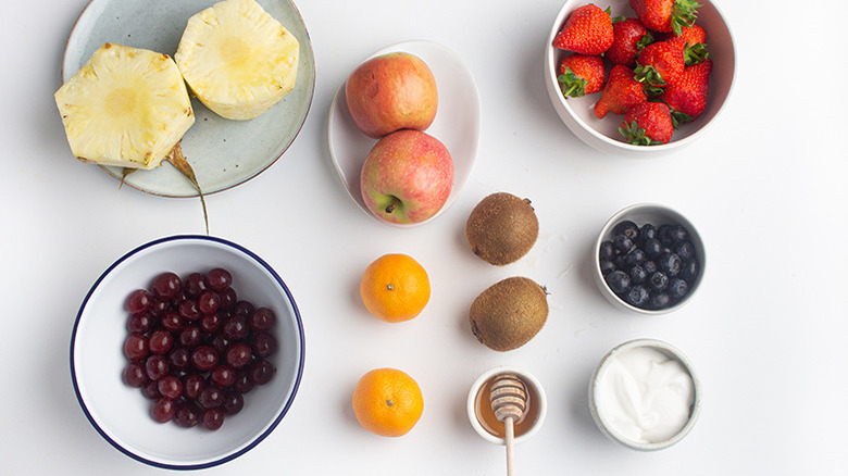 Cut pineapples next to red grapes, apples, tangerines, kiwis, honey, yogurt, blueberries, and strawberries