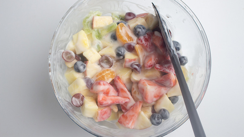 Overhead shot of a glass bowl filled with fruit salad being stirred