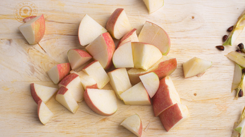 A hand holding a knife over a red apple on a wooden cutting board