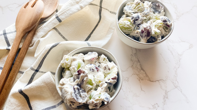 Creamy grape salad with grapes in bowl with wooden serving spoons on counter