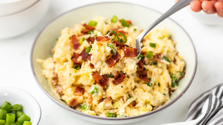 spooning baked potato salad from bowl