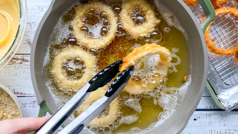 tongs removing onion ring from oil