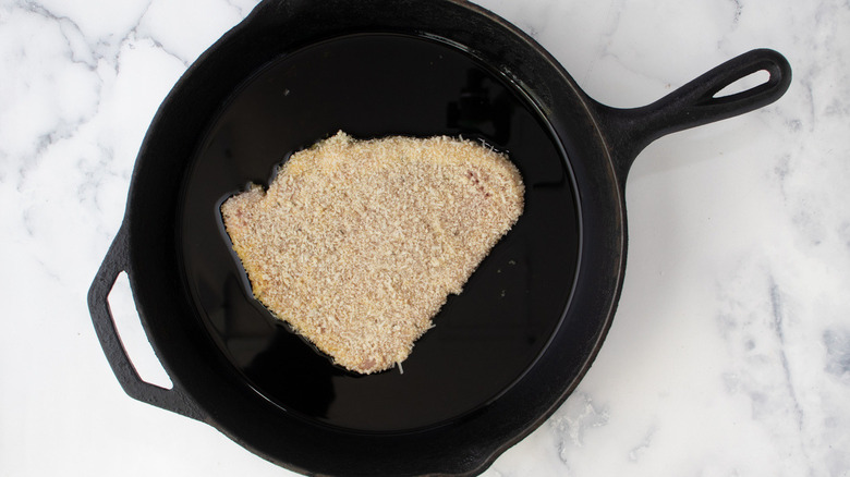 breaded cutlet in a black cast iron frying pan