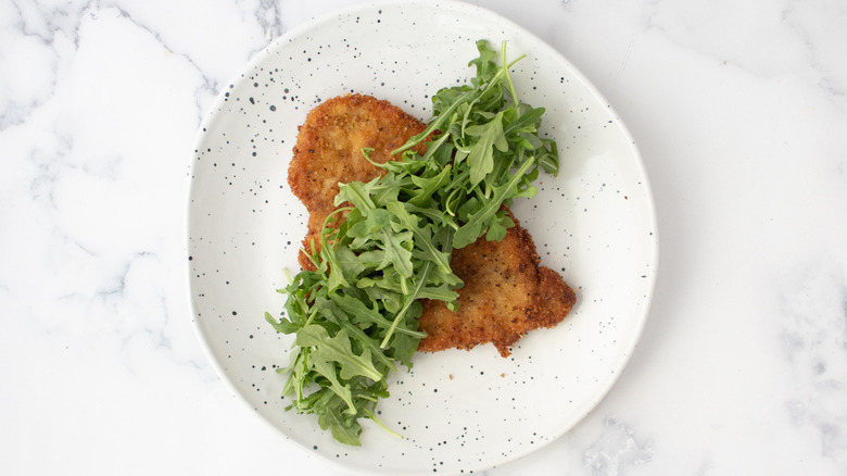 fried breaded cutlet with arugula on a white plate