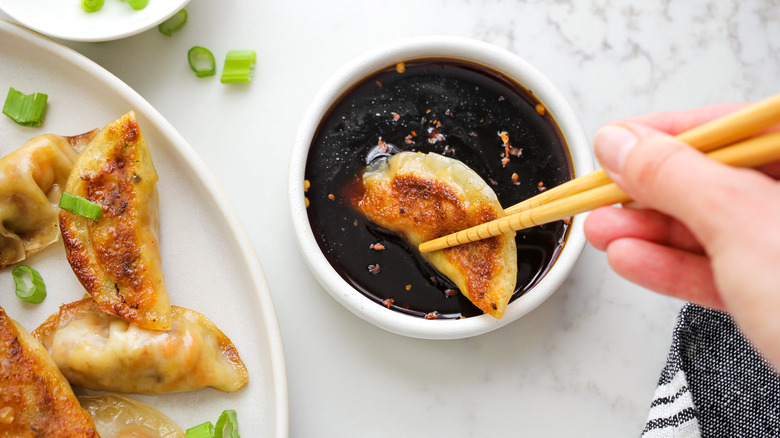 chopsticks dipping dumpling in sauce