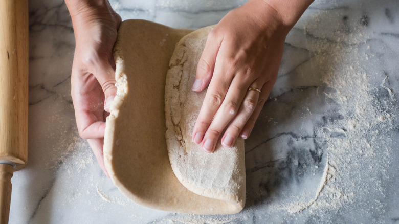 Hands folding dough to laminate