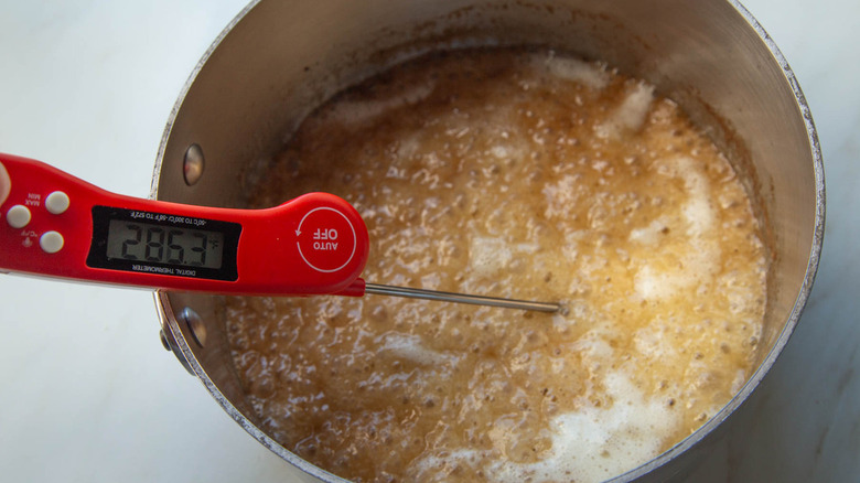 toffee boiling on a stovetop with a thermometer inserted showing 286.3 degrees fahrenheit