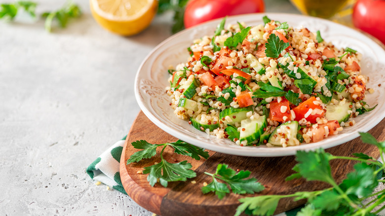 couscous salad in a white bowl with tomatoes, cucumbers and parsley 