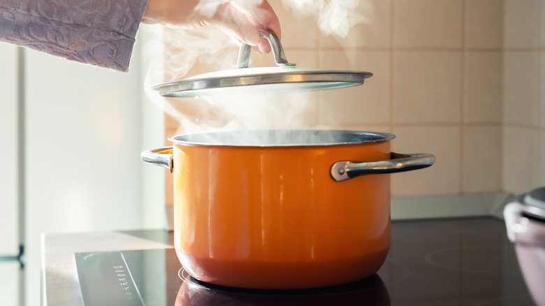 person removing lid on steaming pot