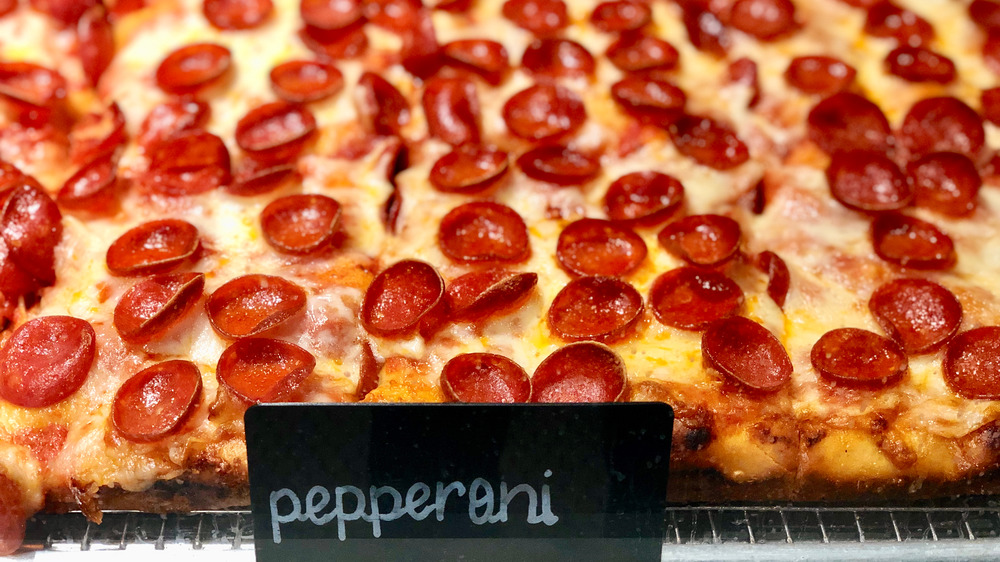 Slices of pizza covered in roni cups in window with "pepperoni" sign