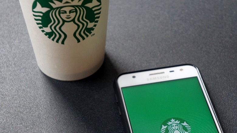 Starbucks hot paper cup next to smartphone open to Starbucks app